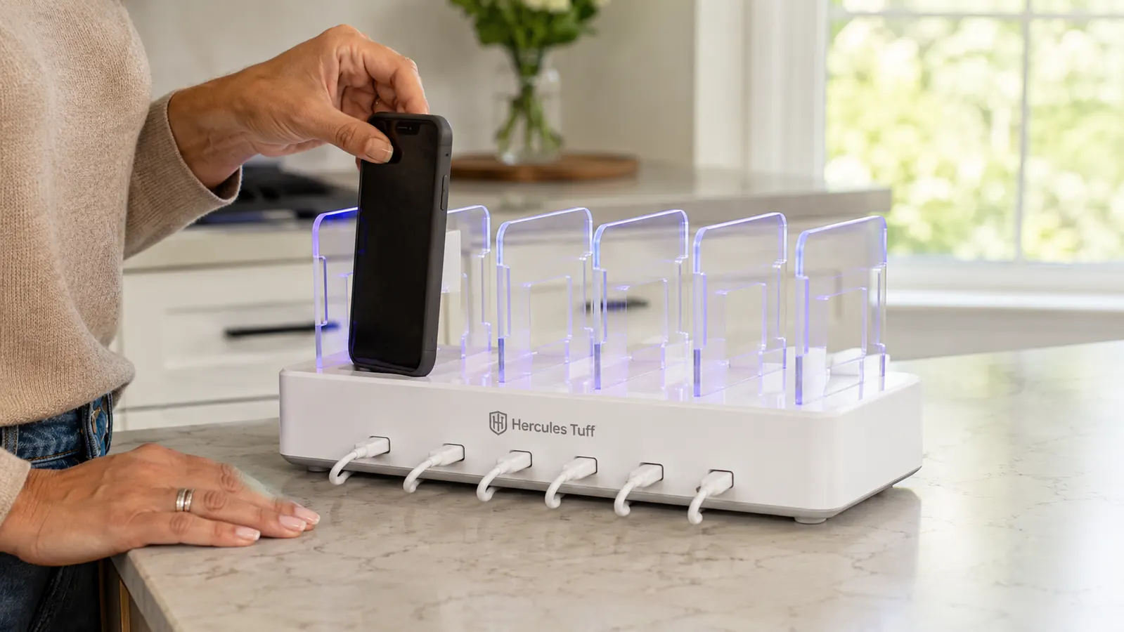 Hand setting a phone into a slot on the Hercules Tuff charging station on a kitchen counter