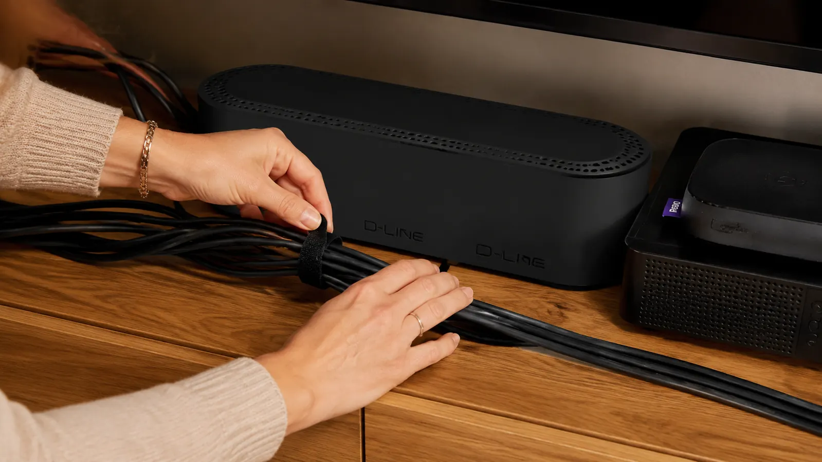 Hand gathering a bundle of TV, cable box, and streaming device cords with a Velcro tie before boxing them up