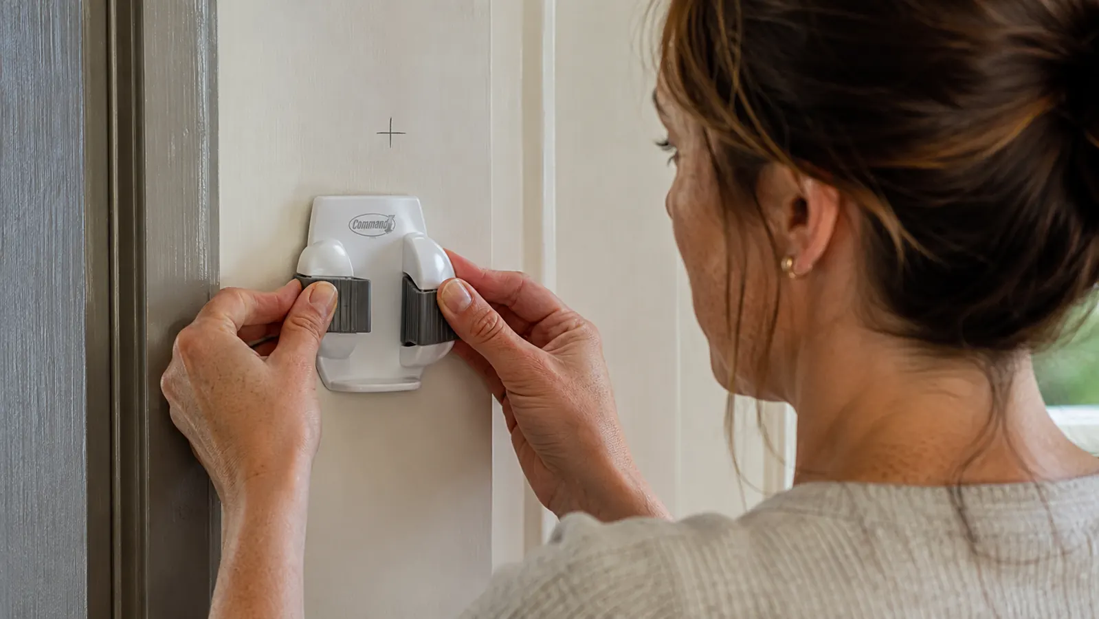 Hand pressing a white Command gripper hook against a marked spot on a laundry room door