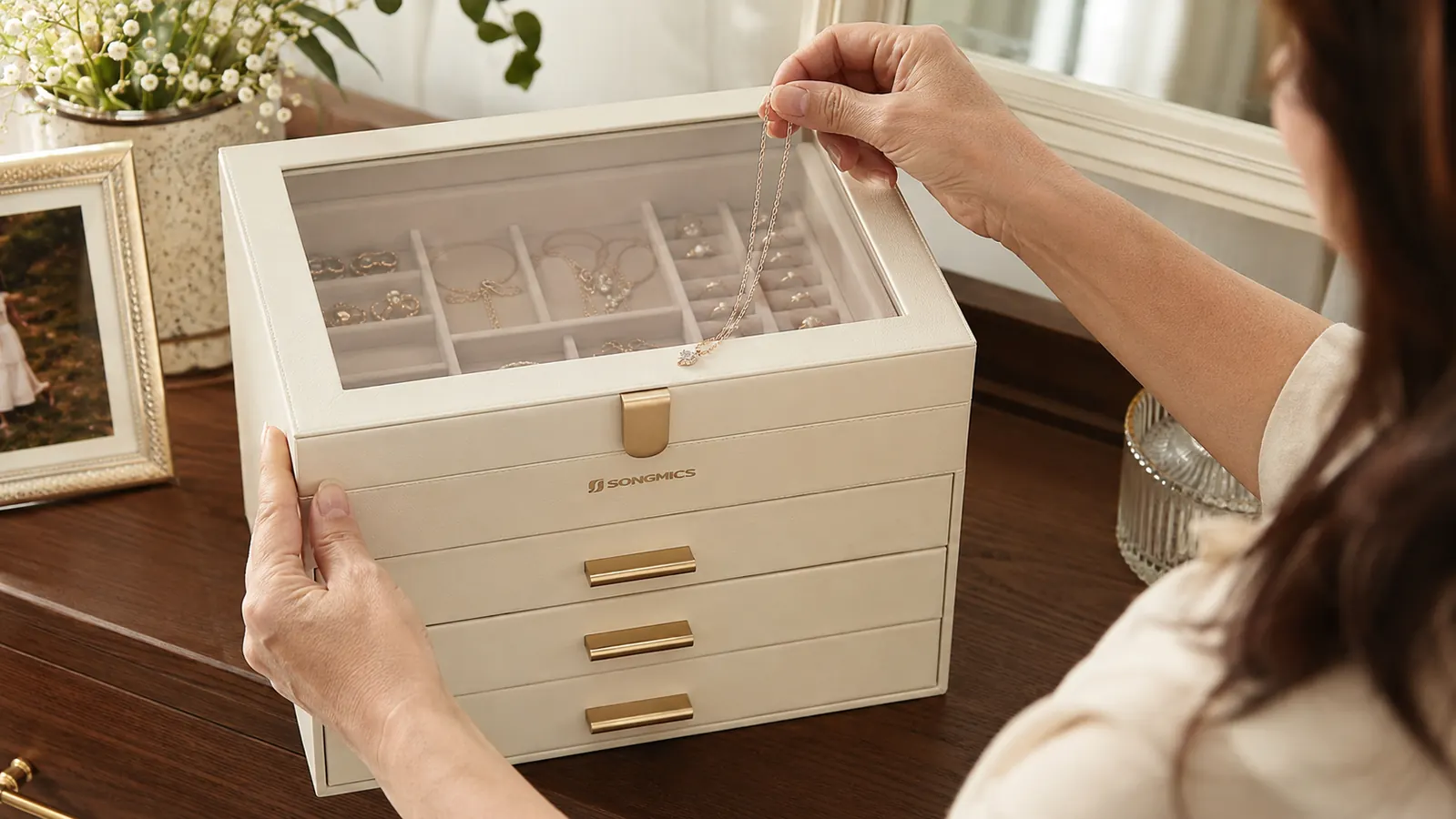 Hands carefully separating and laying untangled necklaces into the SONGMICS glass-lid jewelry box's velvet compartments