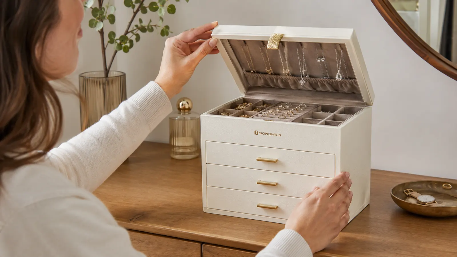 Hand lifting the glass lid of the SONGMICS jewelry box to reach a necklace hook inside